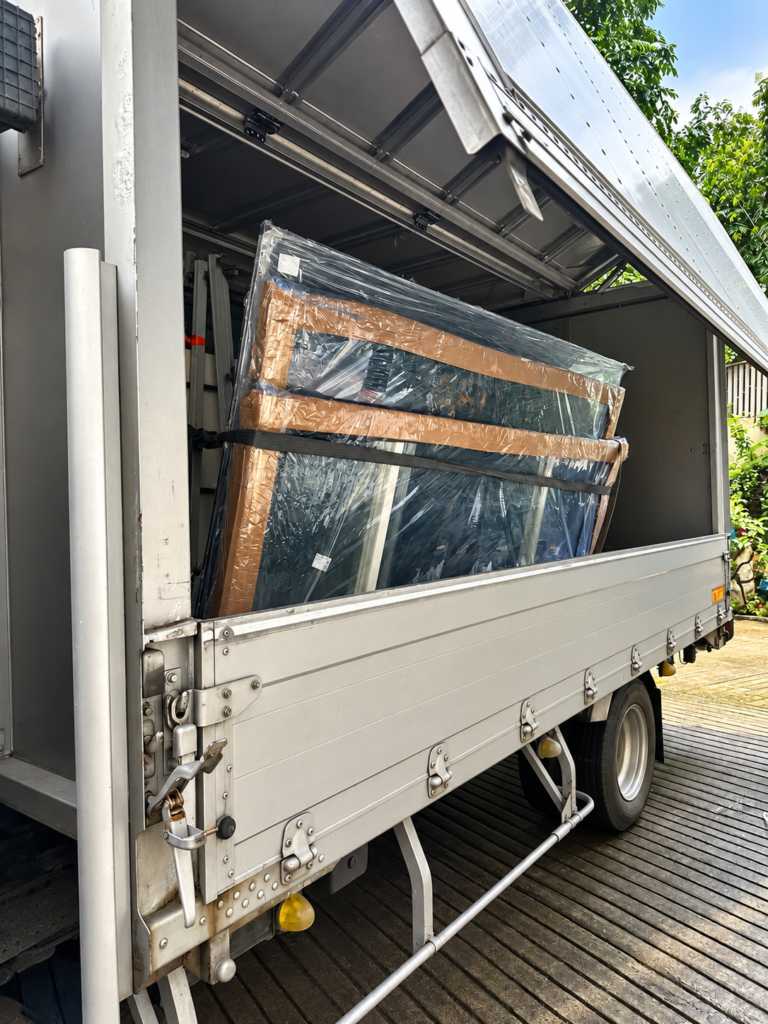 Wrapped glass and aluminium components secured with straps inside a truck.
