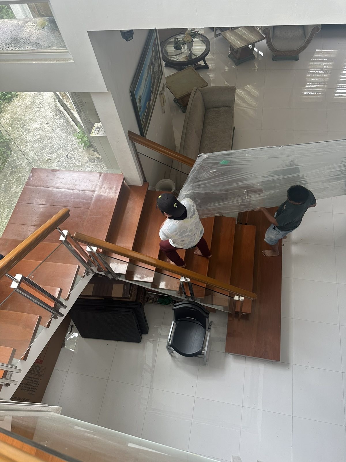 Workers carrying a large wrapped glass panel up an interior staircase.