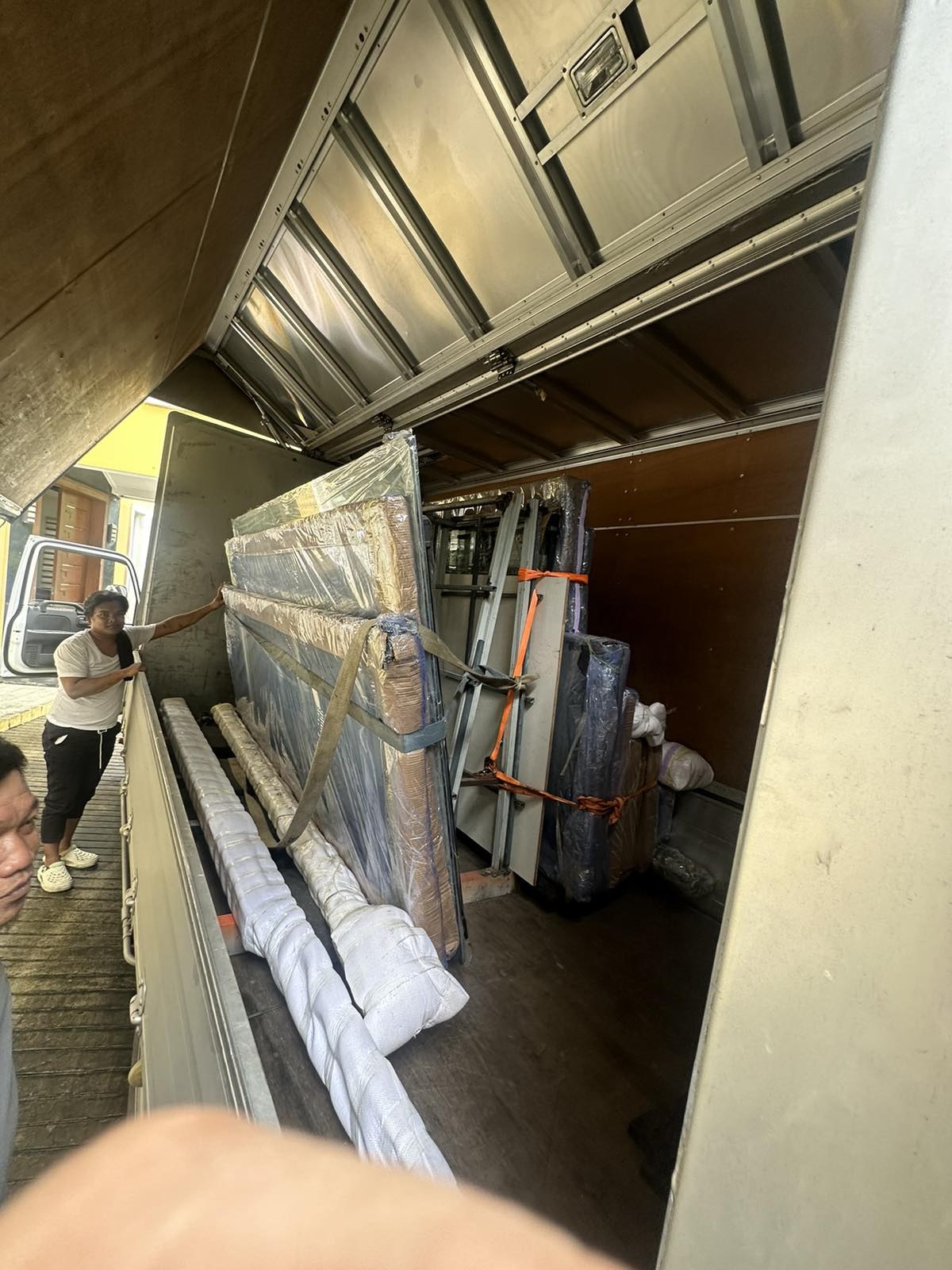 Two workers unloading wrapped glass panels from the back of a truck.